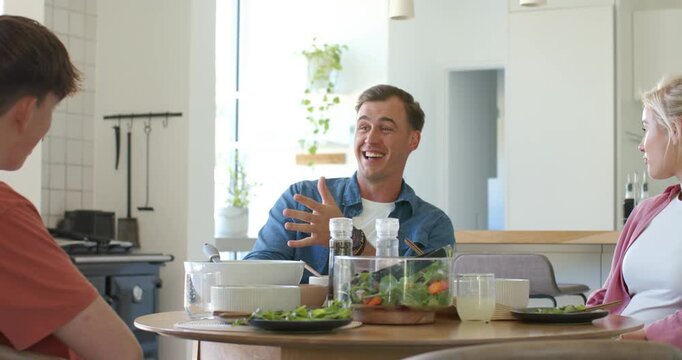 Family with teen son listening while denim shirt father starting story during meal with salad bowl