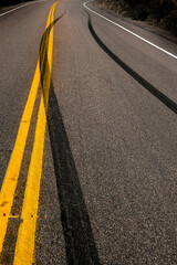 Dark Skid Marks on Asphalt of Road Crossing Yellow Traffic Lines