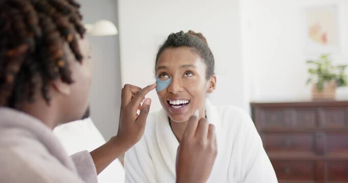 African American couple, partner reaching to apply blue eye patch in bedroom for skincare in robes