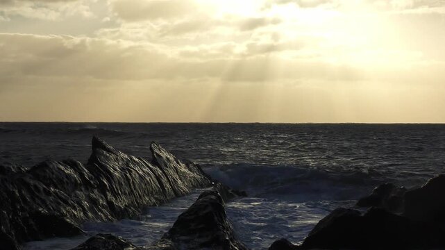 atemberaubender Sonnenuntergang &uuml;ber dem Meer hinter dramatischen Wolken - brechenden Wellen im Abendlicht an felsiger K&uuml;ste, beruhigende Stimmung, inspirierende Landschaft, Reisen, Urlaub
