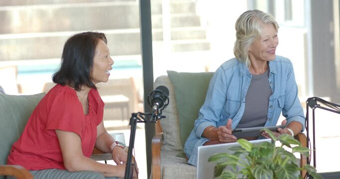 Diverse female hosts recording on sofa in studio third woman entering, moving mics and using tablet