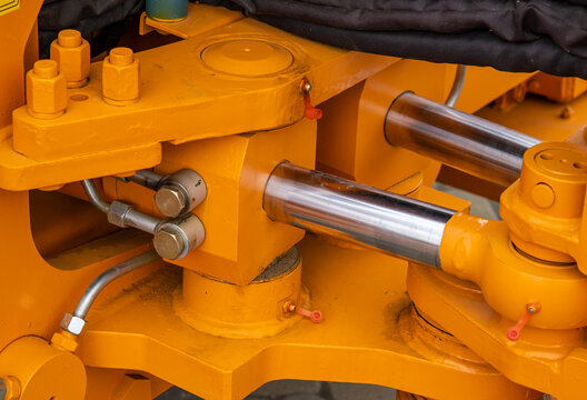 Close-up of powerful hydraulic cylinders and articulated joint on yellow industrial machinery. Detailed view of chrome pistons and pressure lines on a heavy-duty loader or tractor.