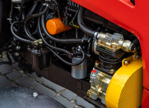 Close-up of a modern red tractor diesel engine with air compressor and fuel filters. Detailed industrial view of a professional agricultural vehicle motor and components for farming machinery.