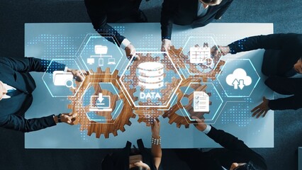 A group of business professionals collaborates around a table, analyzing data with digital...