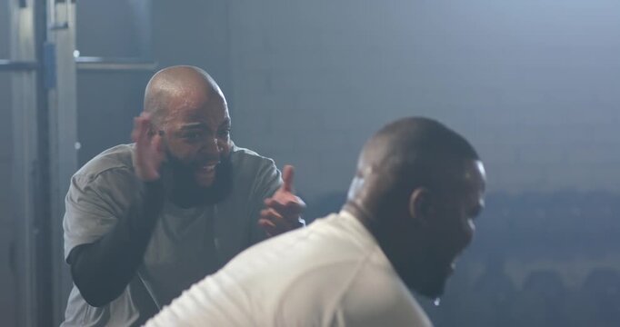 Two African American men, coach clapping and cheering, trainee pulling handle to finish rep at gym