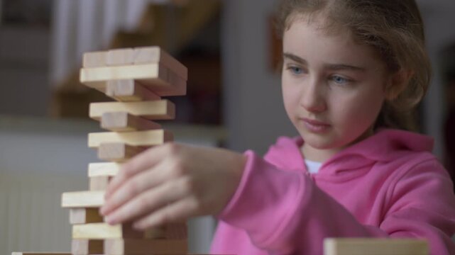 Child Having Fun Building Constructor Tower of Wooden Blocks. Girl Playing Wooden Block Tower Game at Home. Board Creative Game. Child Development Education Leisure. Play With Wooden Building Blocks.