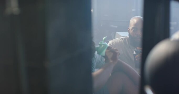 Two African American men front man sharing green bottle through narrow doorway back man sipping mug