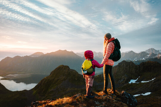 Family hiking in Norway mother and child climbing mountains, parent and kid travel with backpacks enjoying nature views together holding hands lifestyle active summer vacations tour in Lofoten islands