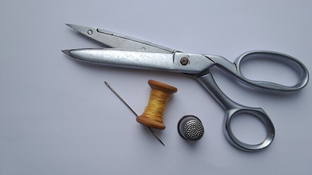 Sewing Tools Set with Scissors, Spool and Needle. Minimal flat lay of tailoring tools including metal scissors, wooden spool, needle and thimble on light background.