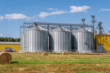 Modern agro-processing plant with silver metal silos for grain storage. Industrial granary elevator complex for drying and cleaning agricultural products against a blue cloudy sky © NastyaPhoto