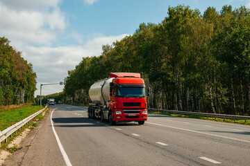 A red truck with a tanker is driving along the highway