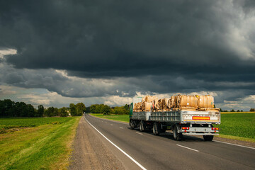 A truck carries bales of hay along the highway, blue clouds in the sky before a thunderstorm © Павел Чигирь