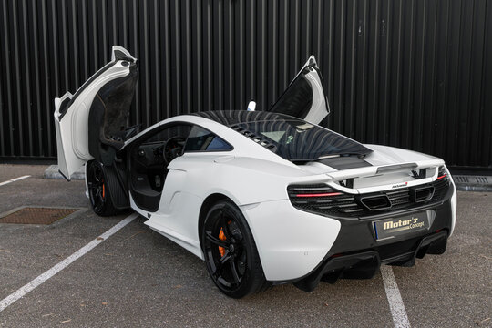 Metz, France - January 21st 2026 : View on a white McLaren 650S with the doors open from 2014 finished in White Pearl Metallic parked on a street in front of a black sheet metal wall.