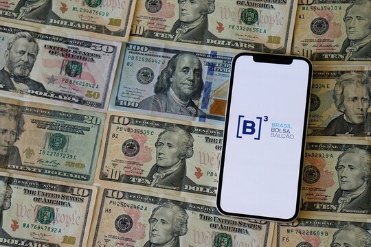 B3 (Brasil Bolsa Balc&atilde;o) logo on a smartphone screen over US dollar bills. Foreign Investment, Brazilian stock market. Ibovespa Brazil. 