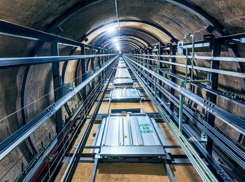 View looking upward from inside a circular elevator shaft, revealing repeating floors with elevator doors on each level.