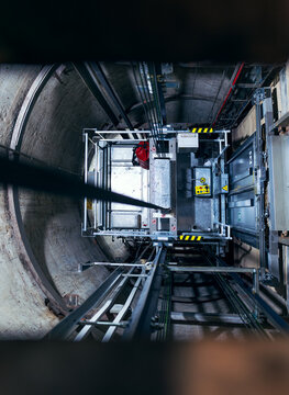 View into an elevator shaft from the machine room, looking down at the elevator car positioned within the shaft.