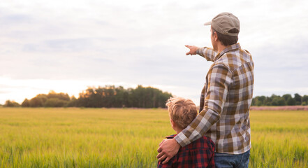 Farmer and his son in front of a sunset agricultural landscape. Man and a boy in a countryside field. Fatherhood, country life, farming and country lifestyle concept.