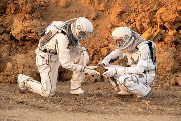 Two astronauts kneeling on the ground and studying a large rock sample together. © Tetiana Tuzyk