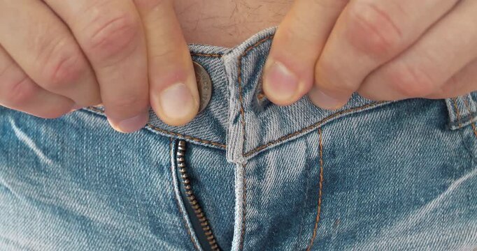 Trying on clothes in a store fitting room. Man can not button his jeans at the waist. The pants size is small and unsuitable. Skinny jeans and a fat belly. Close-up of arms and waist
