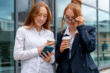 Fototapeta premium Friends check phone and share coffee outside office building in urban area during daytime