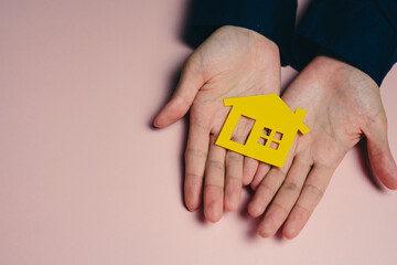 Buying a new house concept. Yellow house symbol held in hands, representing home ownership and real...
