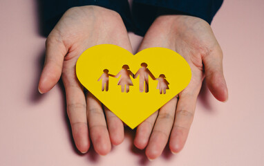 Obraz premium family concept. Hands hold yellow heart symbolizing family love and unity, featuring cut out figures of family. This conveys warmth and connection