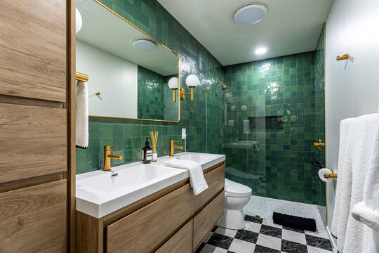 Modern bathroom interior with green tile walls, brass fixtures, double vanity and glass shower enclosure