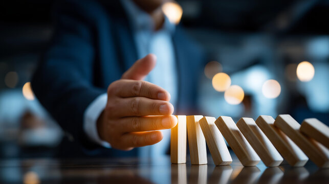Businessman's hand stopping falling dominoes in succession symbolizing effective risk management and crisis prevention strategy business continuity disaster mitigation problem