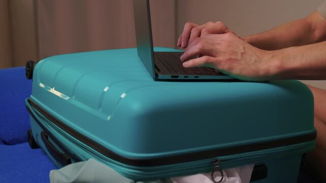 Laptop on turquoise suitcase, hands typing on keyboard on closed case improvised workspace in hotel room with clothes peeking from zip, soft evening light, focused productive mood