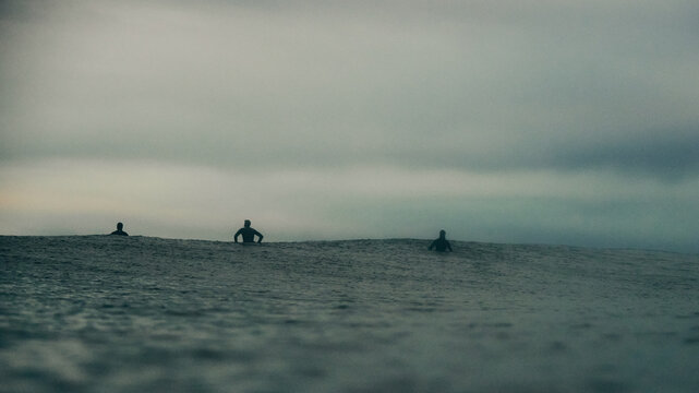 surfers sat on their boards in dark stormy seas
