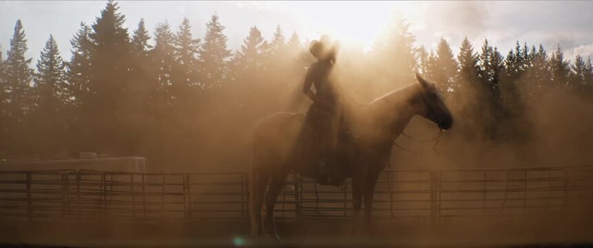 Cowgirl in cowboy hat on horseback, golden hour backlight and dust
