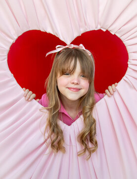 Girl with blonde curls and bangs posing in pink and red Valentine's heart