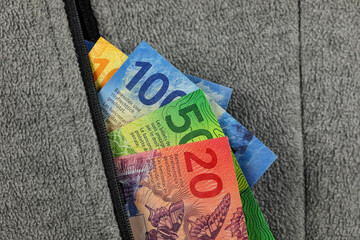 The pocket of the fleece sweatshirt from which Swiss banknotes stick out © marek_usz