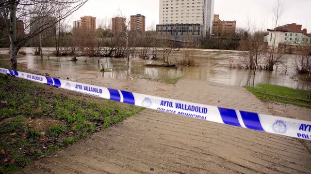 Steady shot shows the pisuerga river receding after a major flood, revealing the muddy riverbanks and a path cordoned off with police tape in valladolid, castilla y leon, spain