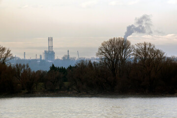 Obraz premium Factory releases smoke near river with trees in the background during cloudy weather
