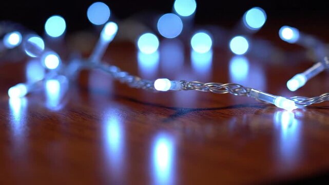Blue led string lights with bokeh effect and bright reflections on a wooden surface, suitable for holiday decoration, festive background, celebration event, and mood lighting.