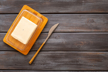 Block of fresh butter in wooden butter dish and a knife, top view
