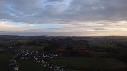 Fototapeta premium Aerial view of green rolling countryside with small village in autumn