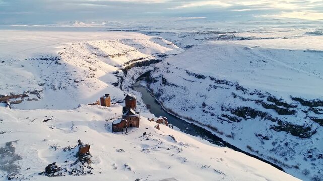 Aerial view of the Menucehr Mosque minaret at Ani Ruins overlooking a snowy canyon in Kars, Turkey. Medieval stone architecture rises above a dramatic winter landscape.