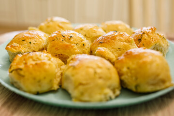 Fototapeta premium Soft garlic herb dinner roll on spatula above plate, shiny butter glaze and fluffy interior, homemade baked bread close up