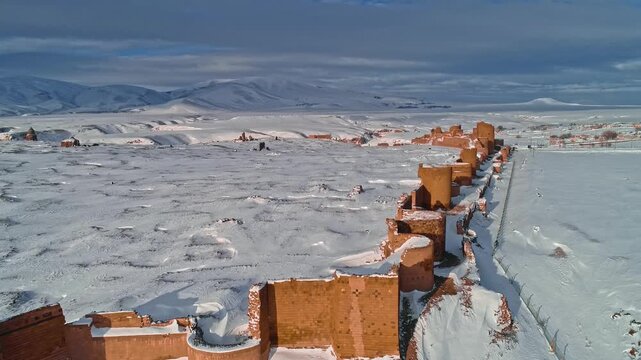 Aerial view of the medieval city walls of Ani in Kars, Turkey. Snow covered defensive towers and stone fortifications stand against a vast winter landscape.