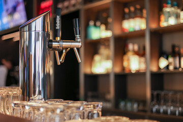 Modern beer tap on bar counter with glassware and blurred bottle background.A polished beer tap stands on a bar counter with clean glasses arranged in the foreground.  © Diatlova Tetiana