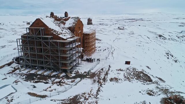 Aerial drone view of tourists visiting Ani Cathedral at Ani Ruins in Kars, Turkey. Snow covered medieval Armenian architecture, historic church structure and winter landscape near the border.