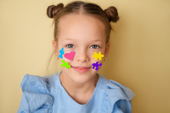 Portrait of smiling child with colorful puzzle stickers and heart on face symbolizing autism awareness. Neurodiversity acceptance, empathy, school support and equal opportunities concept.