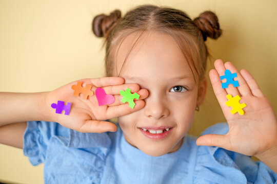 Stickers in the shape of puzzles and hearts decorate the face and palm of a beautiful girl. World Autism Awareness Day. A symbol of education, reason, and people with autism spectrum disorders