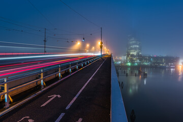 Traffic flows on a bridge in evening mist with city lights reflecting on the water in Sweden