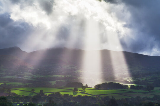 Sunbeams shining through the clouds onto a rural landscape on a stormy summer day, Brecon Beacons, Wales, UK