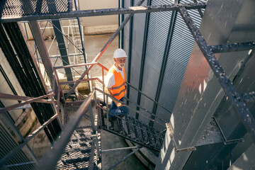 Senior male worker climbing industrial metal staircase at outdoor facility in safety gear