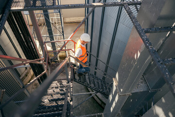 Senior Male Worker in Safety Gear Climbing Industrial Metal Staircase in Outdoor Facility