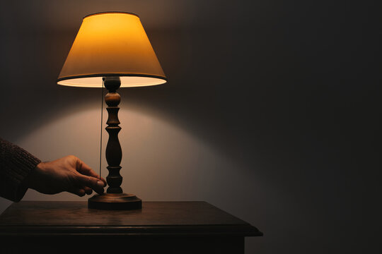 Tactile sensory moment of a hand switching a vintage bedside lamp in the dark, creating a cozy atmosphere and warm ambient glow.